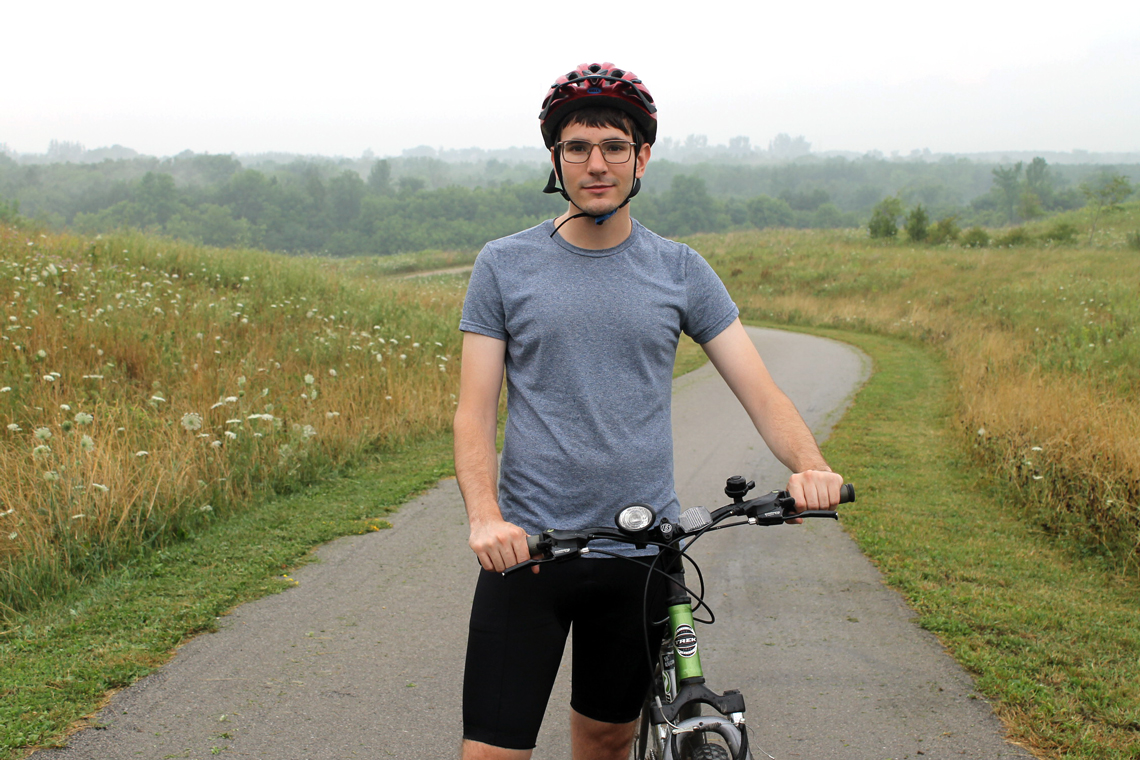Michal stands beside his bike on a trail through a field.