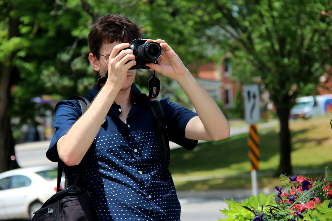 Michal takes a photo with a DSLR camera while standing near a road.