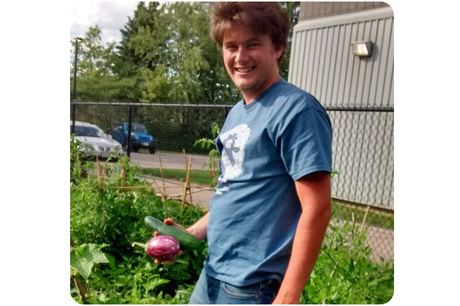 Patrick stands in garden holding vegetables.