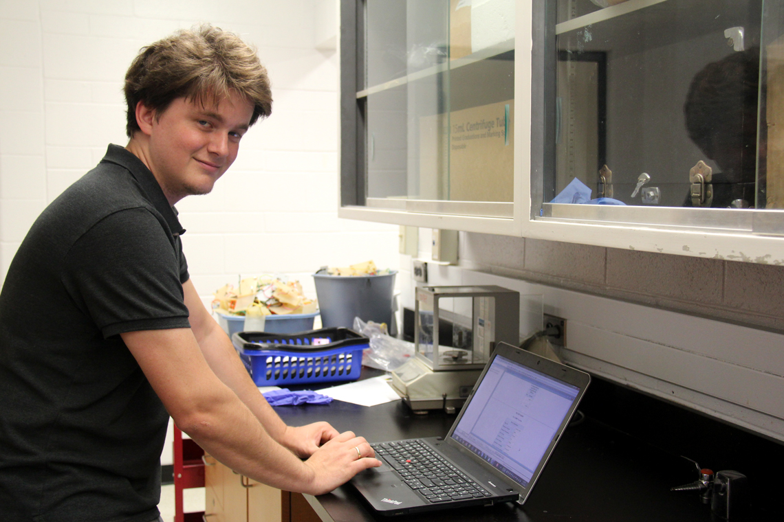 Patrick stands in front of his laptop in a lab.