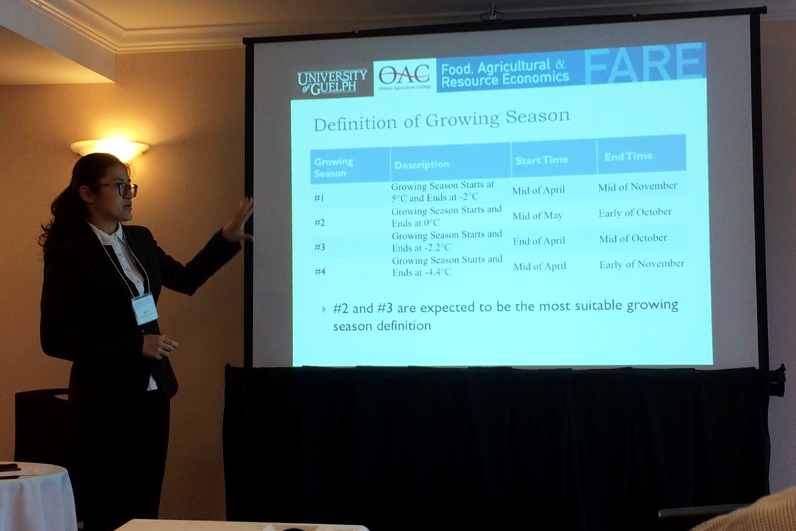 Qin stands in front of a large screen, presenting at a conference.