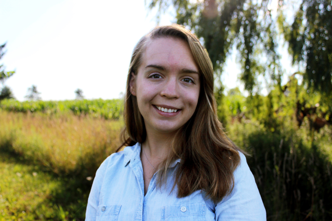 Rachael Coon stands outside, in front of a field.