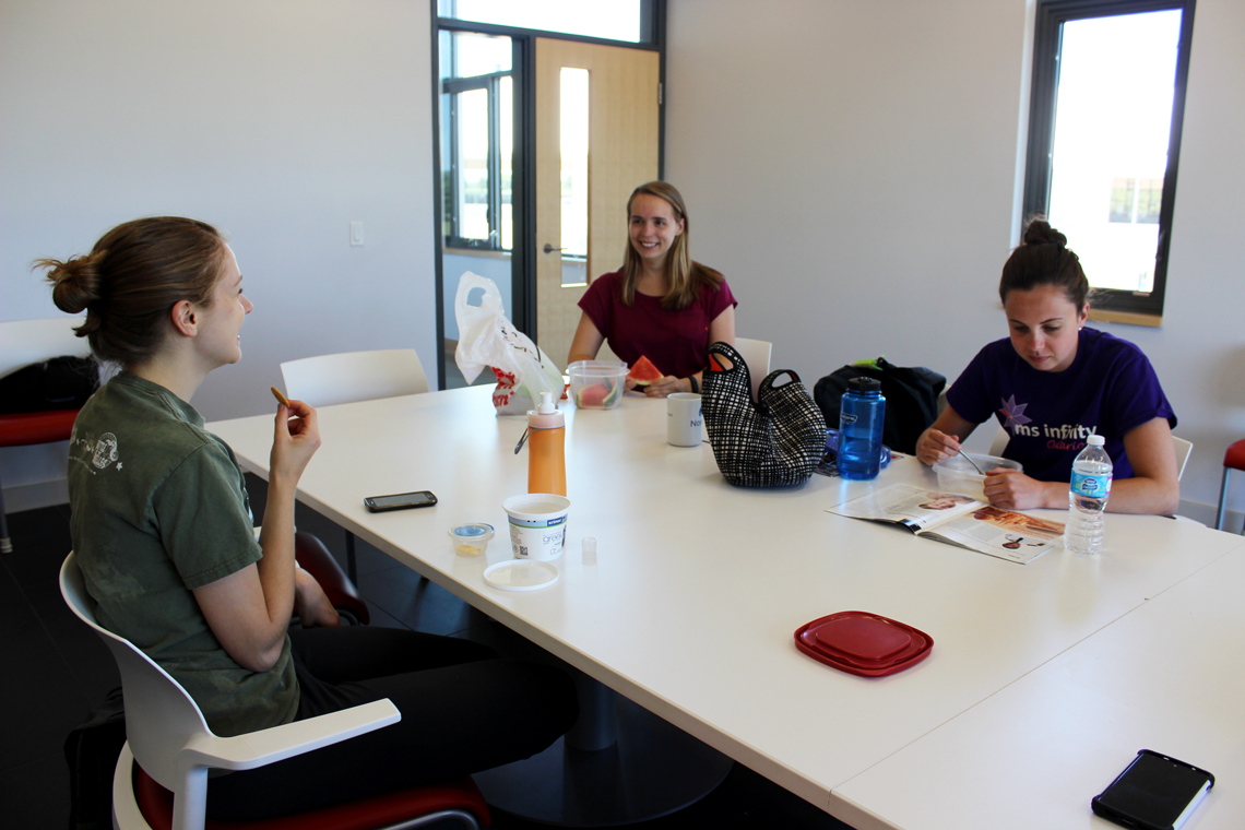 Racheal eats lunch with two other coworkers at a white table.