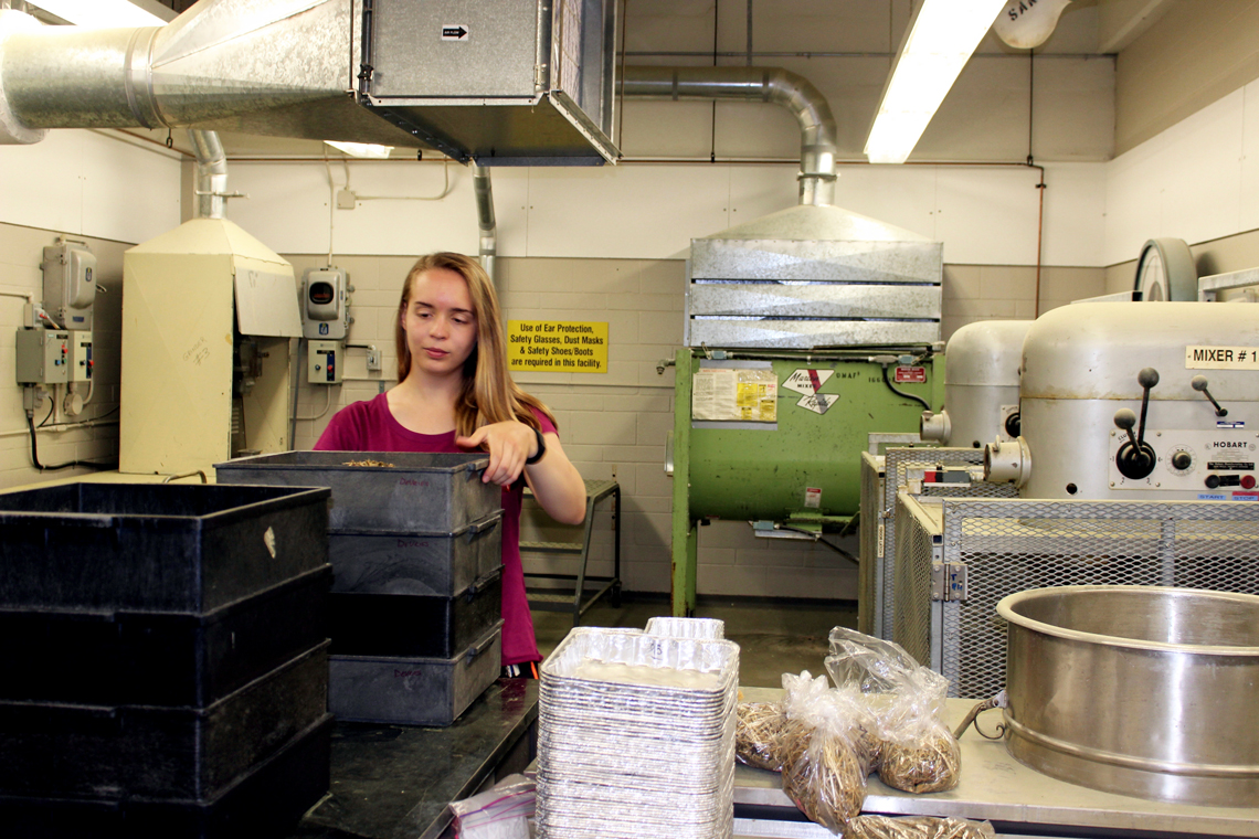 Rachael holds a black tray of feed samples in a large lab.