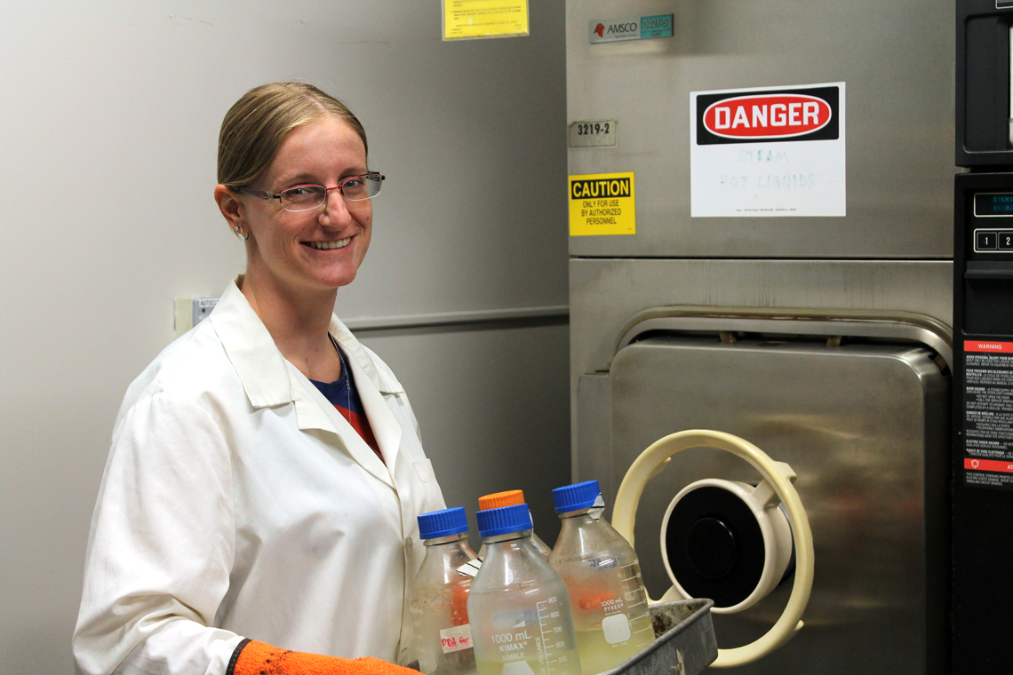 Sara holds a tray of glassware in front of the autoclave.