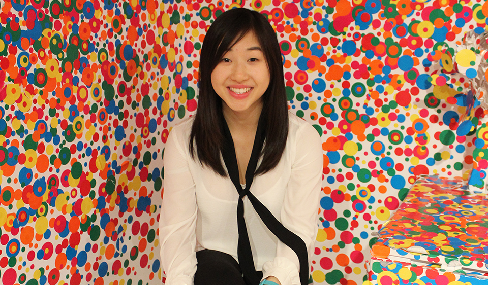 Stephanie sits at an art exhibit with colorful dots on the walls.