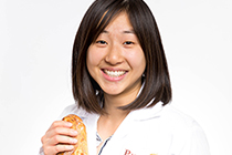 Head shot of Stephanie in a lab coat holding a loaf of bread.