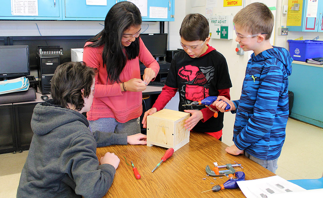 Four students build bumble bee nest boxes in a classroom. 