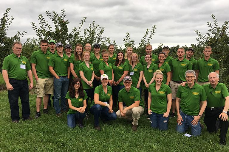 A large group of students and coaches stand and kneel in an orchard.