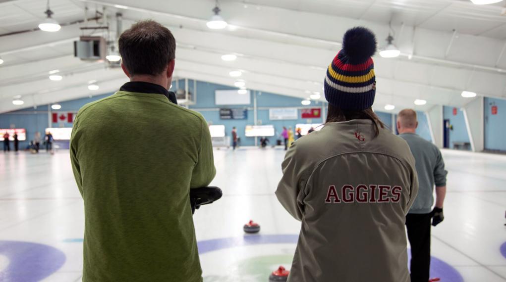Male and female Aggies look out at curling ice