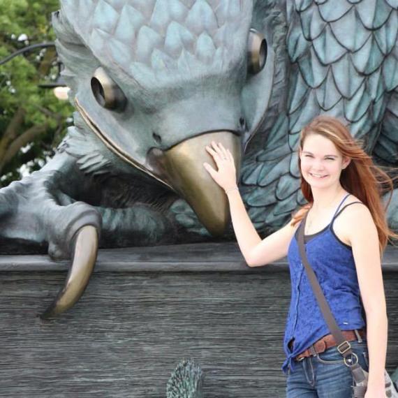 Glenna stands with hand on beak of large Gryhon statue