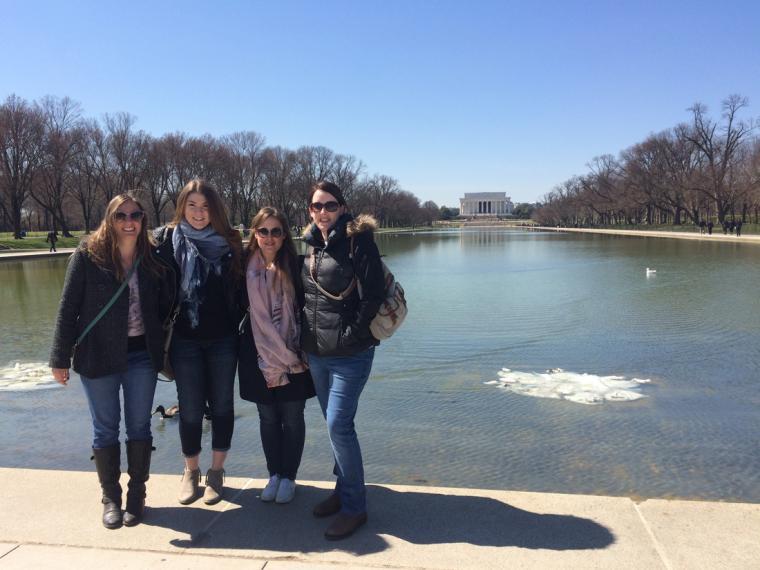 Four female students stand in front of the large pond in front of the Masters students in front of the Lincoln Memorial at the National Mall