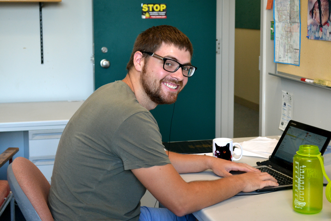 Zach sits at desk with laptop.