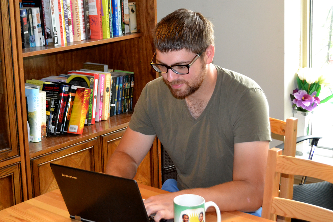 Zach sits at table with laptop and cup of coffee.
