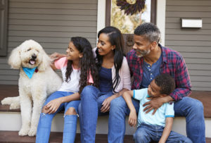 Family With Children And Pet Dog Sit On Steps Of Home