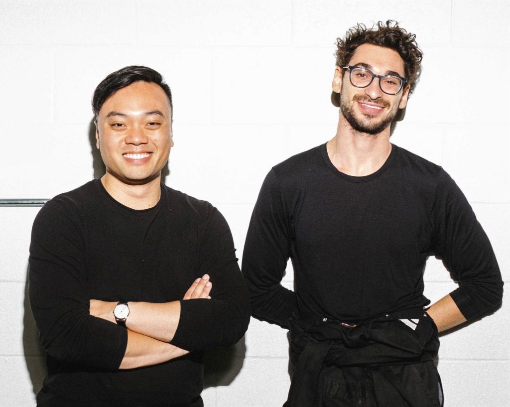 two men in black smile at camera