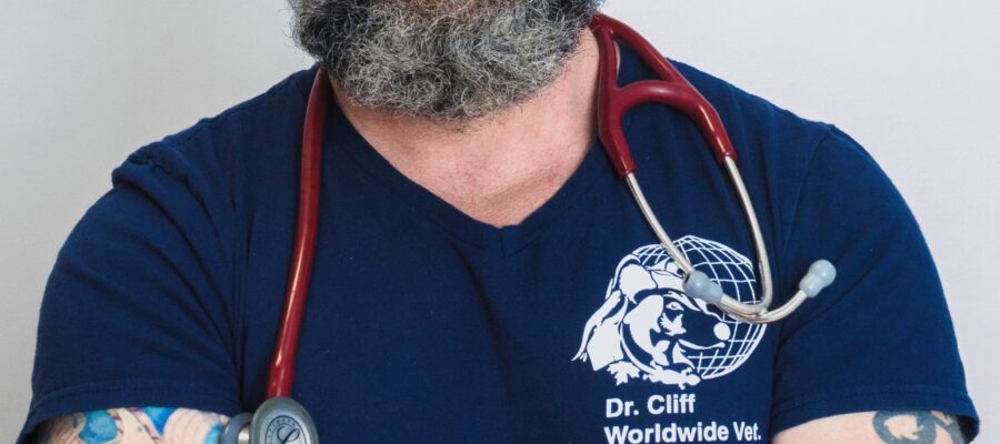 bearded man in T-shirt with stehescope smiles at camera