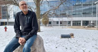 Dr. Doug Larson sits on a rock outside a building in the winter