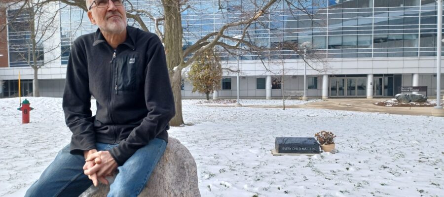 Dr. Doug Larson sits on a rock outside a building in the winter