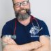 bearded man in T-shirt with stehescope smiles at camera