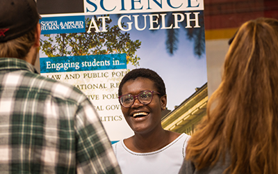 Student smiling and talking to two other students in front of a banner
