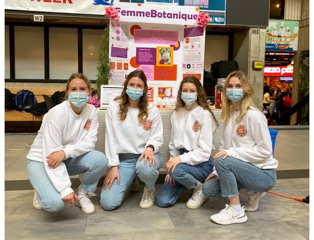 Four team members of Femme Botanique kneeling in their matching light blue jeans and white sweaters in front of their display at the Project SOY Plus finale. 