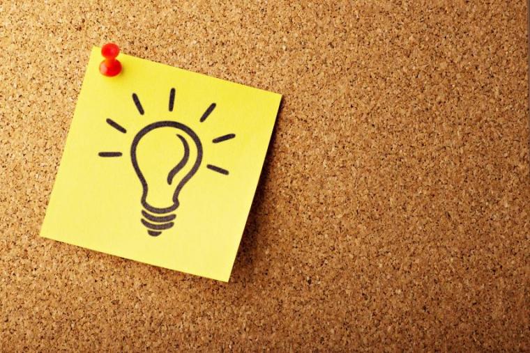 Lightbulb drawn on a yellow sticky note, pinned to a corkboard with a red thumbtack.
