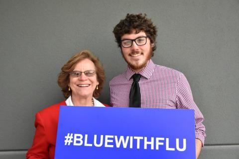 Photo of Cate Dewey and Adam Beswick holding a #bluewithflu sign