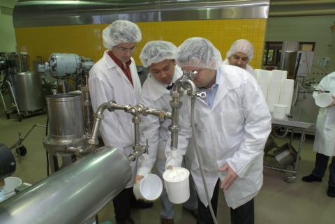 Photo of three people wearing lab coats and head coverings look at ice cream coming out of a faucet