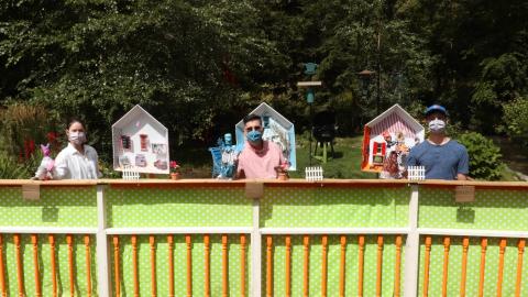 Three people wearing masks and holding puppets on an outdoor theatre set