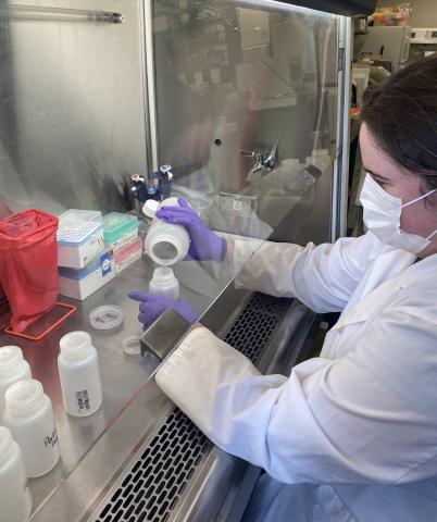 A woman in a lab pouring liquid from one bottle to the next