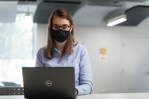 A woman wearing a mask and typing on a laptop