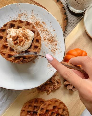 A plate of pumpkin spice waffles with a hand cutting into them with a knife