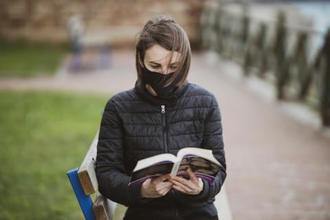 A woman wearing a mask and reading a book
