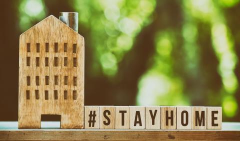 A wooden house on the left with wooden blocks on the right that say, "Stay home."