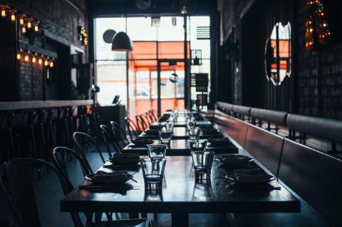 A photo of an empty restaurant with a row of tables and chairs and an empty bar.