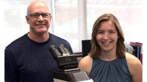 Drs. Geoff Wood and Latasha Ludwig standing in front of a microscope together.