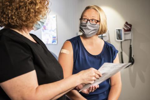 A woman talking to a nurse in a doctor's office after getting a vaccine.