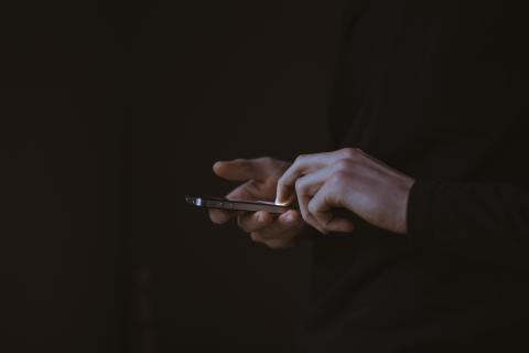 A person wearing a black sweatshirt and holding an iPhone.