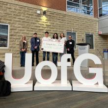 Winners of Project Soy Plus standing with a cheque in front a U of G sign
