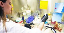 A woman in a lab coat with gloves on working with samples.