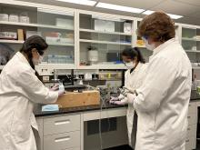 Three people wearing white lab coats and masks testing a blue mask on a machine
