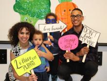 A family standing together with signs and vegetable cut outs in the background.