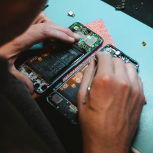 An iPhone that has been opened with someone's hands working on the inside of the phone