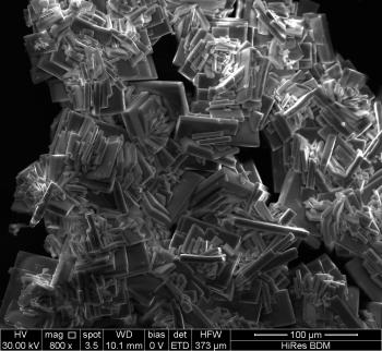 Through a scanning electron microscope, a black and white photo of almost book shaped grey crystals on a black background.