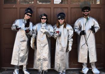 Four women standing in front of a garage wearing aluminum-rayon coats, spats, and kevlar gloves that give a sci-fi aesthetic 