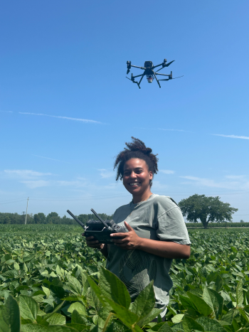 A woman standing in a field with a drone flying overhead.