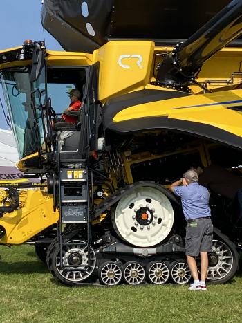 Someone sitting in the cabin of a yellow tractor with someone else standing outside, leaning onto it.