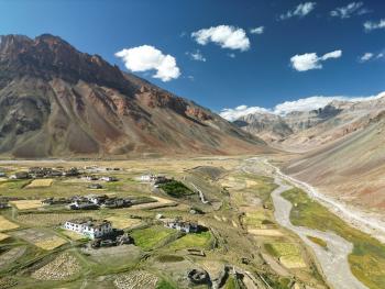 The village of Sking with mountains in the distance and to the left with a some buildings and harvested fields in between.