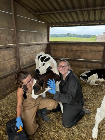Two women posing with black and white calf.